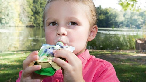 un enfant boit une compote de fruits. Il est préférable de donner des fruits classiques aux enfants car les gourdes de fruits à boire sont trop mauvaises pour la santé.